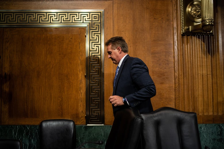 Flake, head down, walking behind chairs in the Kavanaugh hearing room.